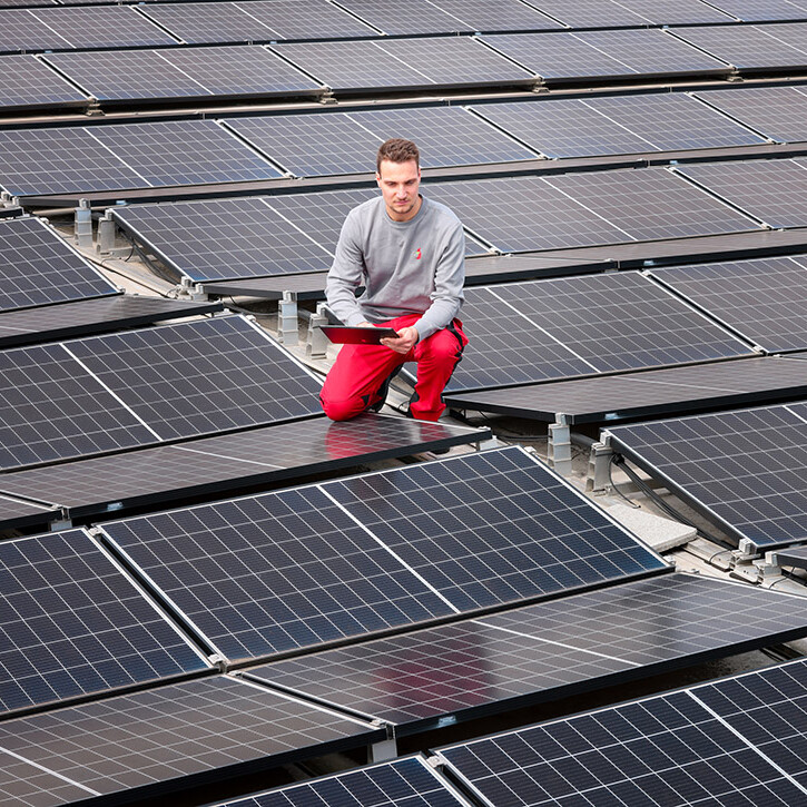 Ein Mann kniet auf einem Dach mit einem Laptop neben Solarpaneelen.